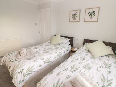 A bedroom with two single beds with plant patterned bedding and beige towels on each bed at 54 Croft Court in Tenby