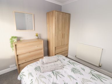 A bedroom with a wooden wardrobe chest of drawers a mirror and a bed with fern patterned bedding at 54 Croft Court in Tenby