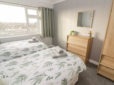 A bedroom with two single beds with leaf patterned bedding a wooden dresser with plants and a mirror at 54 Croft Court in Tenby