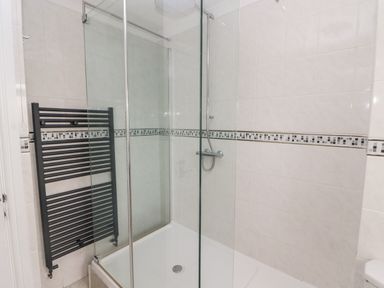 A bathroom shower area with tiled walls a glass door and a black towel radiator at 54 Croft Court in Tenby