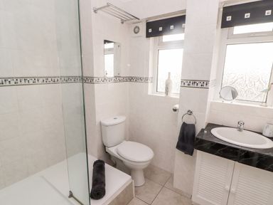A bathroom with a shower area, a toilet, a sink with a black countertop, and two windows at 54 Croft Court in Tenby