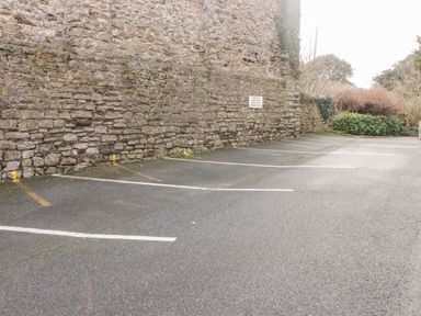 An empty parking lot with marked spaces next to a stone wall and plants at 54 Croft Court in Tenby
