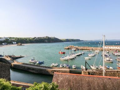A harbor with multiple boats and a stone pier by the sea with cliffs and buildings in the background at 54 Croft Court in Tenby