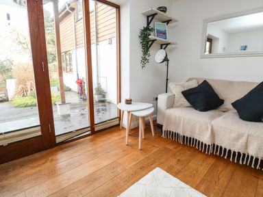A seating area with a sofa covered by a throw blanket and cushions beside nested side tables and large glass doors at Little Rondeval in Totnes
