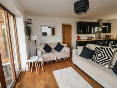 A living room with beige sofas with cushions a small white table wooden floor and black kitchen cabinets at Little Rondeval in Totnes