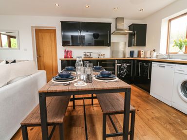 A kitchen with black cabinets a wooden table set for four and white appliances at Little Rondeval in Totnes