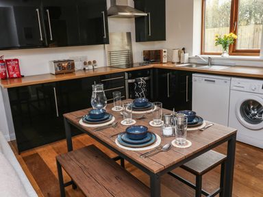 A kitchen with black cabinets wooden countertops a wooden dining table set for four with blue dishes glasses and cutlery at Little Rondeval in Totnes