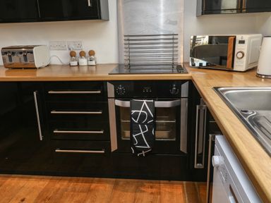 A kitchen countertop with a toaster coffee sugar and tea jars an oven with a towel a microwave kettle and a sink at Little Rondeval in Totnes