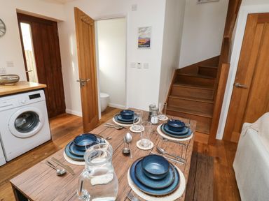 A dining area with a wooden table set for four with blue plates and bowls next to a washing machine and wooden stairs at Little Rondeval in Totnes