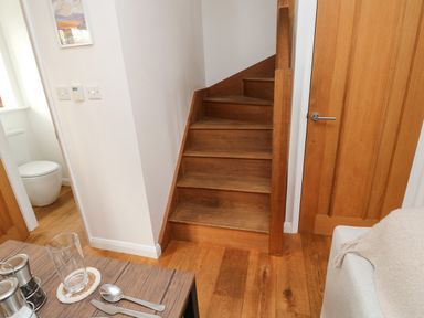 Wooden staircase next to a wooden door with a dining table and cutlery in the foreground at Little Rondeval in Totnes