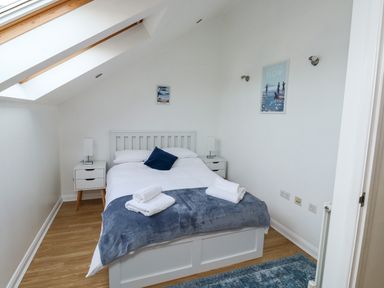 A bedroom with a bed bedside tables a blue rug and skylight windows at Little Rondeval in Totnes