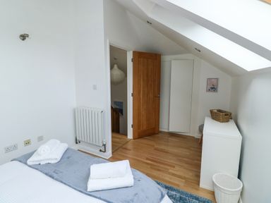 A bedroom with a bed and towels folded on it a wooden door a white cabinet and skylight at Little Rondeval in Totnes
