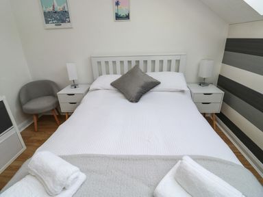 A bedroom with a double bed two bedside tables with lamps a gray chair and towels on the bed at Little Rondeval in Totnes