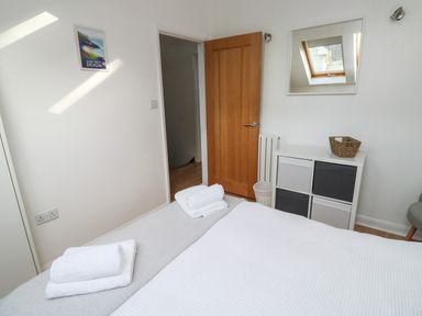 A bedroom with a bed, towels on the bed, a wooden door, a storage unit with fabric drawers, a wall mirror, and a small basket at Little Rondeval in Totnes