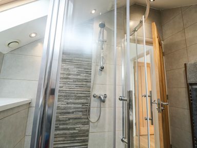 A shower area with glass doors wooden door and tiled walls at Little Rondeval in Totnes