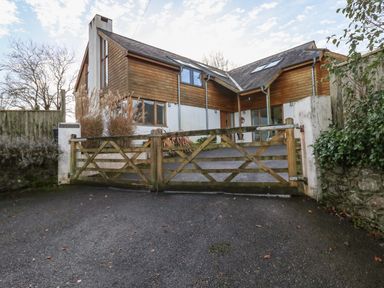 A modern house with wooden cladding behind a closed wooden gate at Little Rondeval in Totnes