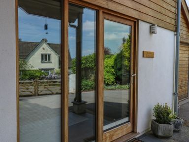 A wooden framed glass door with adjacent window and plants outside at Little Rondeval in Totnes