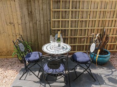 An outdoor seating area with a mosaic table surrounded by four metal chairs with blue cushions at Little Rondeval in Totnes
