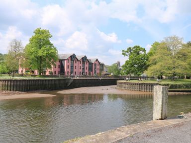 A river with a concrete embankment and pink buildings with trees along the bank at Little Rondeval in Totnes