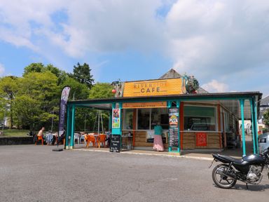 An outdoor cafe kiosk with a sign reading Riverside Cafe with tables and chairs outside and a motorcycle parked nearby at Little Rondeval in Totnes