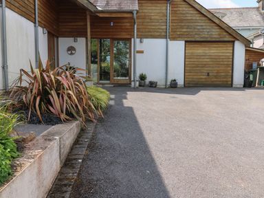A driveway with a wooden garage door and a glass entrance door with plants on the side at Little Rondeval in Totnes