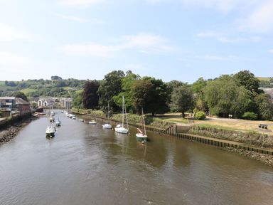 A river with sailboats docked along the shore and trees lining the riverbank at Little Rondeval in Totnes
