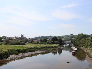 A river with boats on the right side and a small town with a church on the left side across the river at Little Rondeval in Totnes