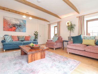 A living room with blue and pink sofas cushions a wooden coffee table and abstract painting at Riviere Barton in Hayle