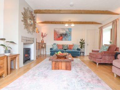 A living room with a blue sofa pink armchairs a wooden coffee table and wall art at Riviere Barton in Hayle