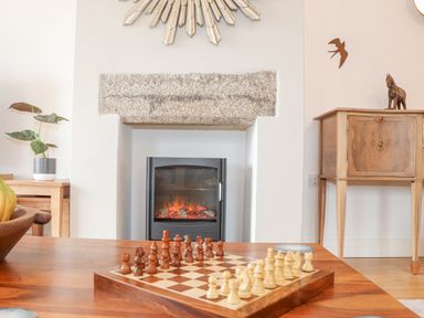 A chessboard on a wooden table with a fireplace, a plant, and wooden cabinet at Riviere Barton in Hayle