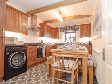 A kitchen with wooden cabinets a washing machine an oven a dining table with chairs and a window at Riviere Barton in Hayle