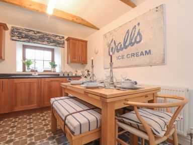 A kitchen with wooden cabinets a dining table set for four with candles and a wall sign reading coralls ice cream at Riviere Barton in Hayle