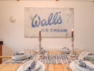 A dining table set with plates glasses candles and napkins under a wall sign saying Walls ice cream at Riviere Barton in Hayle