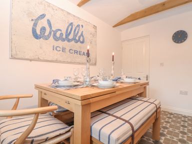 A dining area with a wooden table set for six with striped cushions on chairs and bench at Riviere Barton in Hayle