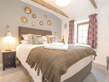 A bedroom with a bed pillows a blanket nightstand lamps window with curtains and decorative mirrors on the wall at Riviere Barton in Hayle
