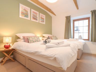 A bedroom with two single beds white bedding bedside table with lamp artwork above bed and a window with curtains at Riviere Barton in Hayle