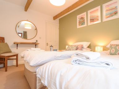 A bedroom with two single beds white bedding and towels wooden chair round mirror on wall at Riviere Barton in Hayle