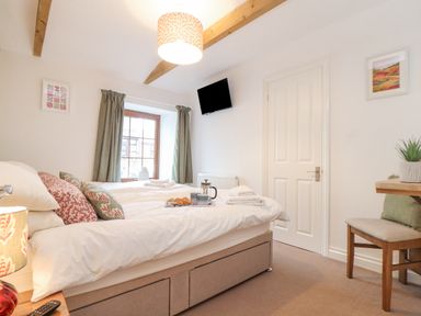 A bedroom with a bed with pillows and a tray with coffee and pastries in front of a window with curtains and a wall-mounted television at Riviere Barton in Hayle