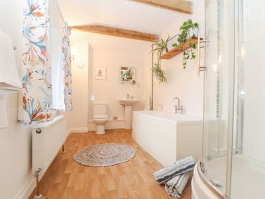 A bathroom with a bathtub toilet sink shower wooden floor and plants on a shelf at Riviere Barton in Hayle