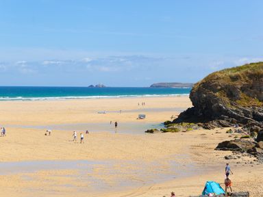 A sandy beach with people walking and relaxing near rocky cliffs and ocean at Riviere Barton in Hayle