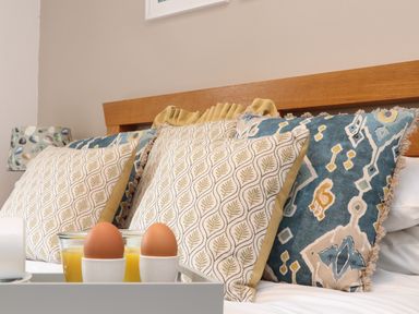 A bed with patterned cushions and a tray holding two boiled eggs and a glass of orange juice at Riviere Barton in Hayle