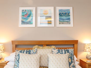 A bedroom with a wooden headboard pillows on the bed and three framed artworks above the bed at Riviere Barton in Hayle