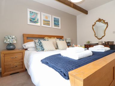 A bedroom with a wooden bed frame, patterned pillows, bedside tables with lamps, folded towels on the bed, a vintage mirror, and framed artwork at Riviere Barton in Hayle
