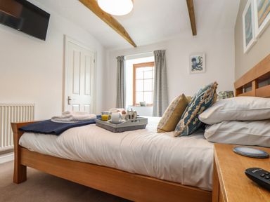 A bedroom with a wooden bed frame pillows and breakfast tray near a window at Riviere Barton in Hayle