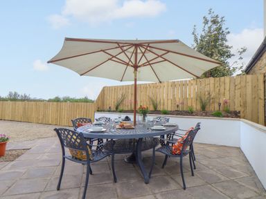 An outdoor patio area with a round table and six chairs under a large white umbrella at Riviere Barton in Hayle