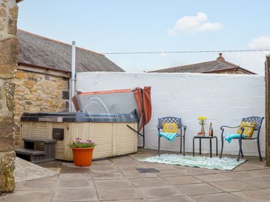 An outdoor patio with a hot tub a potted plant two chairs with cushions and towels and a small table with flowers and drinks at Riviere Barton in Hayle
