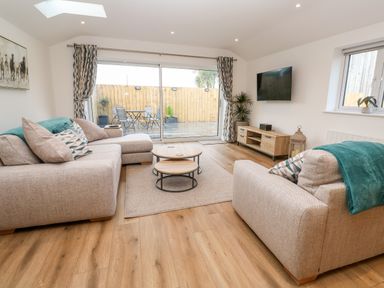 A living room with two beige sofas a wooden coffee table and a mounted TV at Puffins Rest in Goldsithney