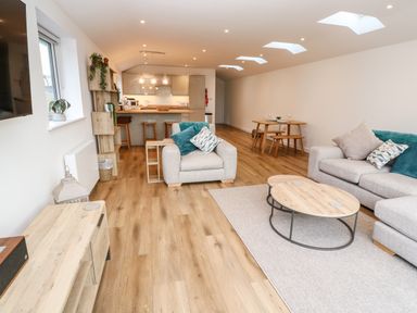 An open plan living room with sofas coffee tables dining table stools and kitchen area at Puffins Rest in Goldsithney