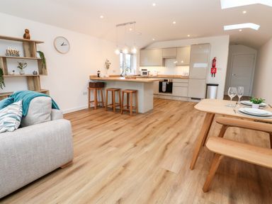 A kitchen and dining area with island stools a dining table and a sofa at Puffins Rest in Goldsithney