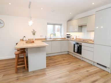 A kitchen with wooden countertop seating bar and stools built in oven microwave and refrigerator at Puffins Rest in Goldsithney